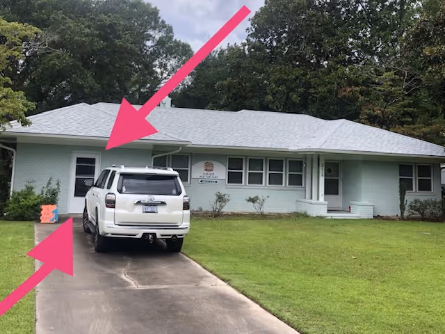 Front view of a light-green, single-story building with a driveway and a white SUV.