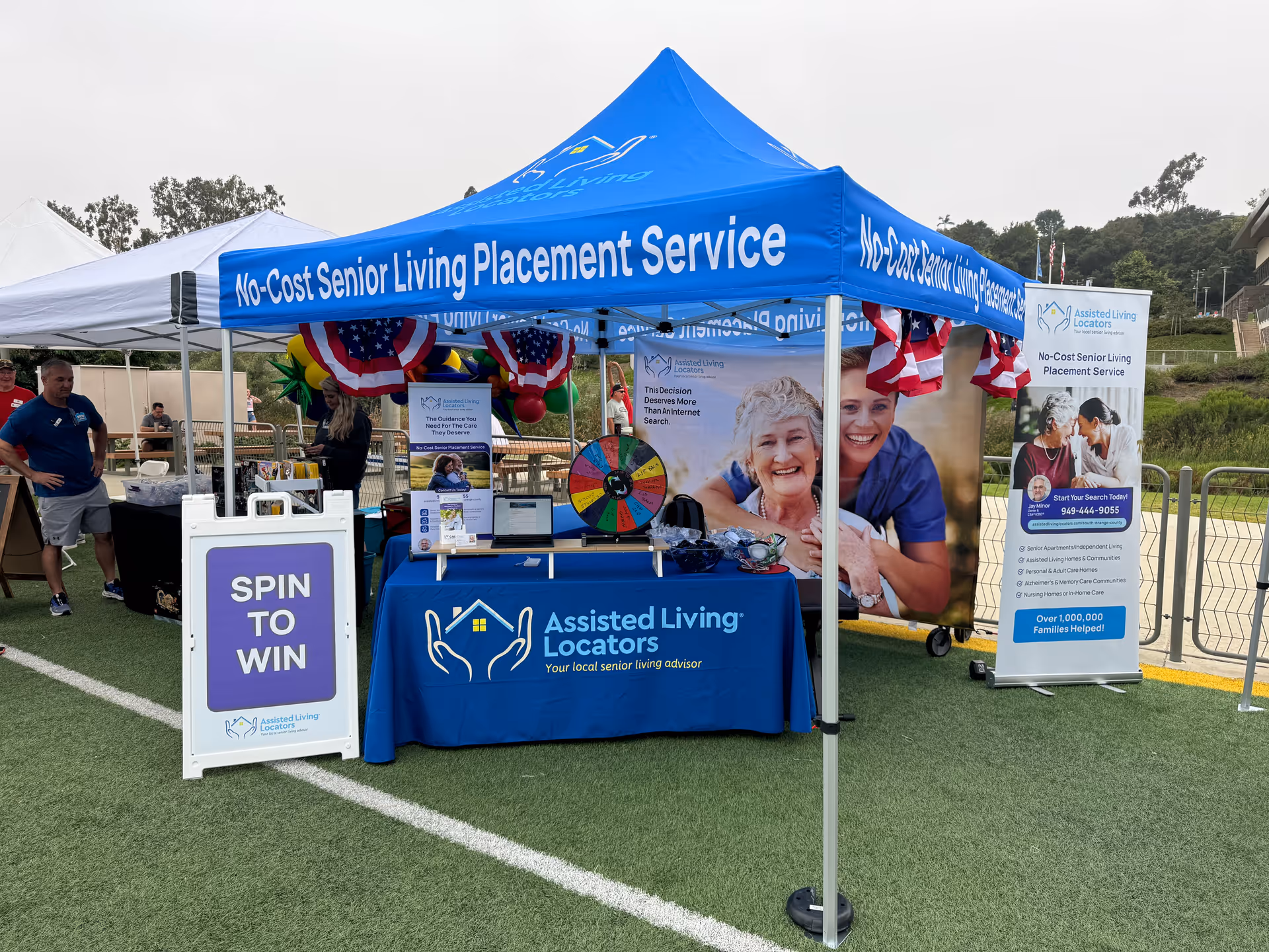 Outdoor booth for Assisted Living Locators with banners, spin-to-win wheel, and tables
