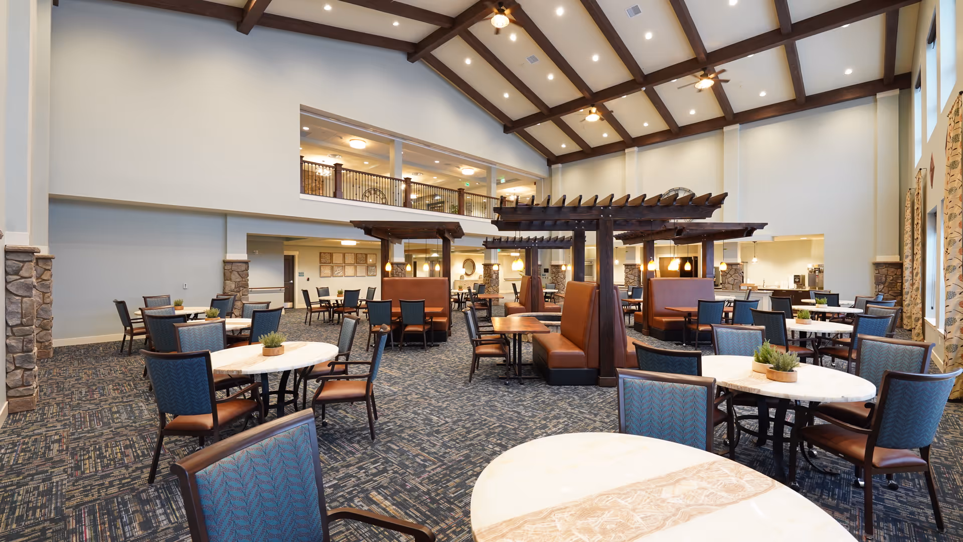 Spacious senior living dining room with round tables, blue chairs, and wooden beams.