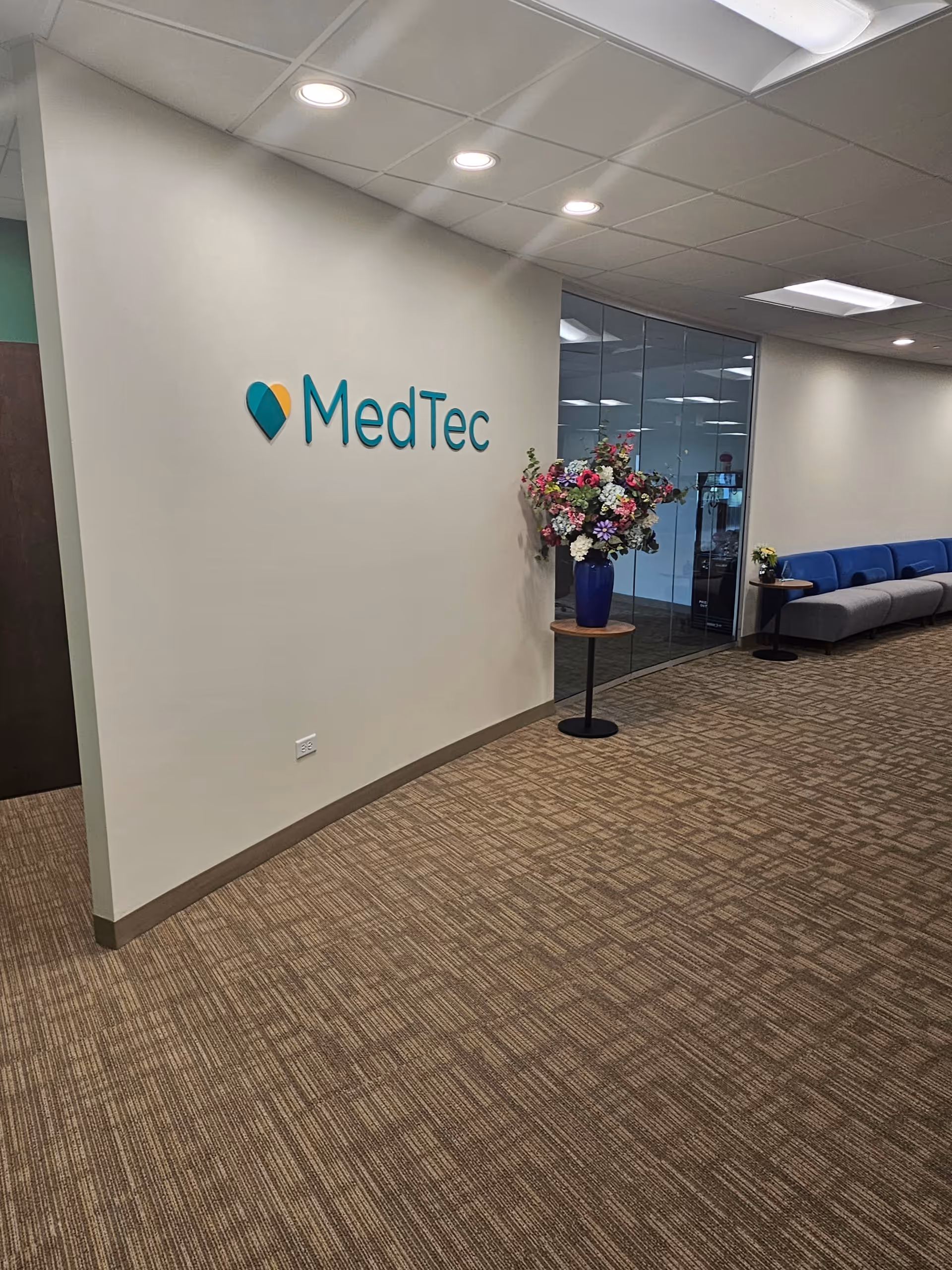 Lobby interior of MedTec facility featuring sign, flower arrangement, and blue seating.