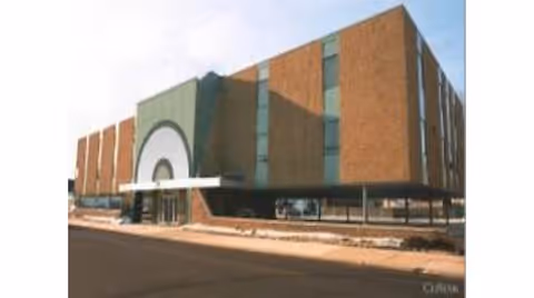 Exterior view of a brick building with green accents and a curved entrance.