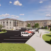 Front exterior of a multi-story senior living facility with a parking lot, several parked cars, and a walkway to the entrance under a partly cloudy sky.
