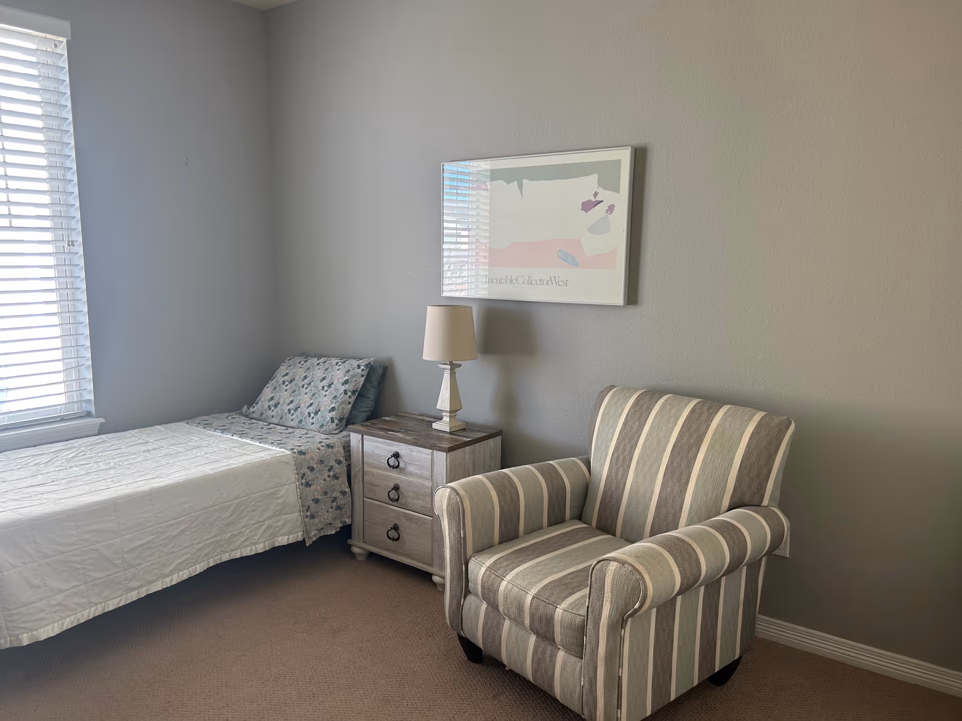 Bedroom with single bed, nightstand, lamp, and striped armchair by the window.