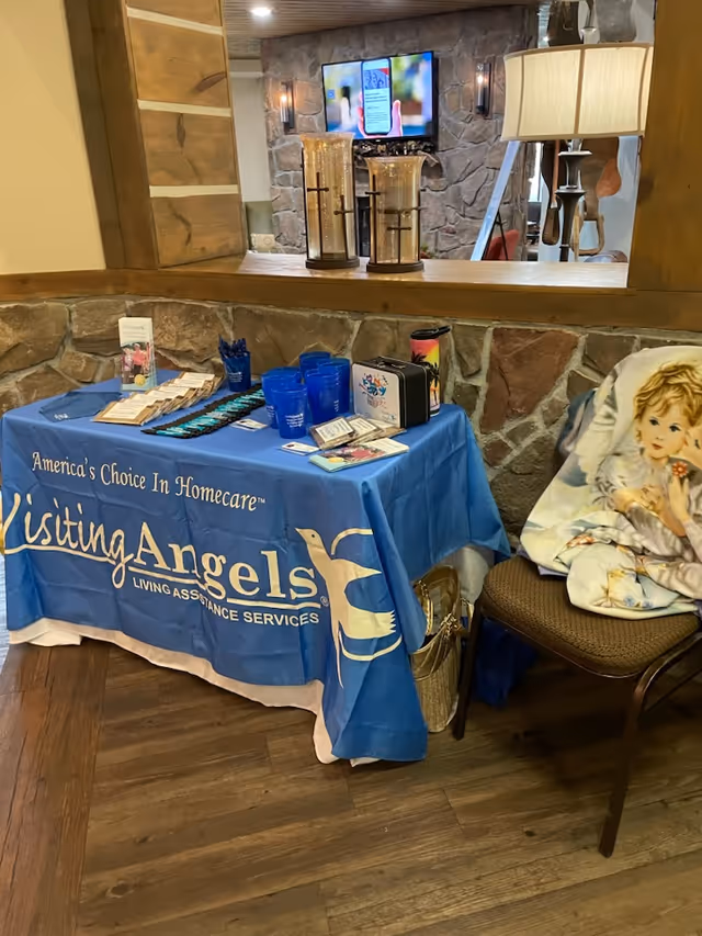 Blue tablecloth table display for Visiting Angels with brochures in a stone-walled indoor lounge.