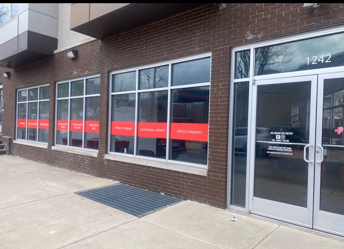 Exterior brick storefront with tall windows and a red signage band along front.