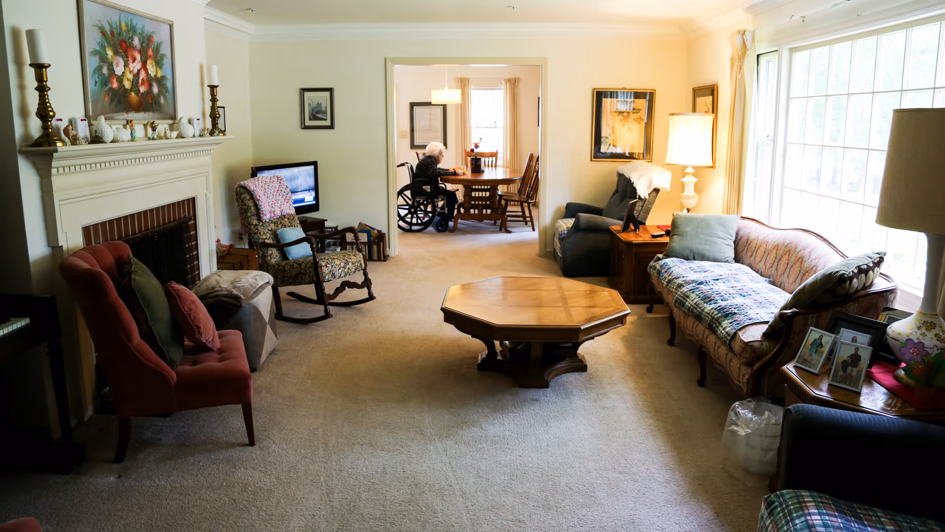 Spacious living room in a senior care center with sofas, chairs, and a central coffee table.