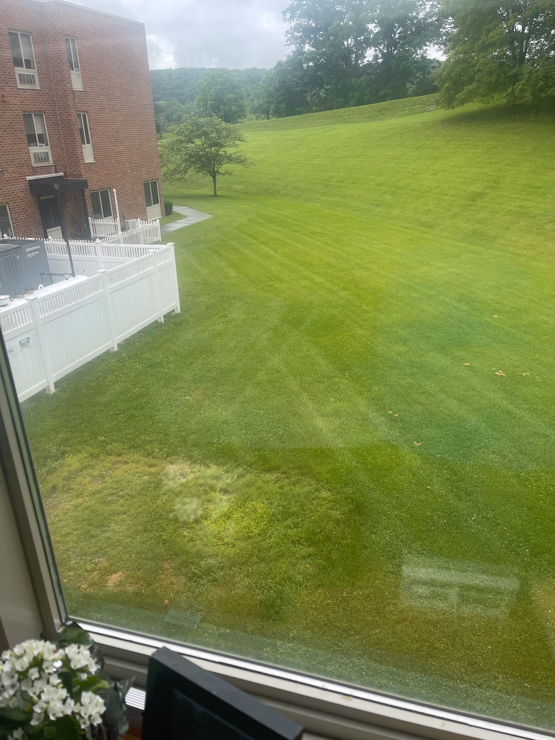View from a window of a brick building overlooking a white fence and expansive grassy lawn.