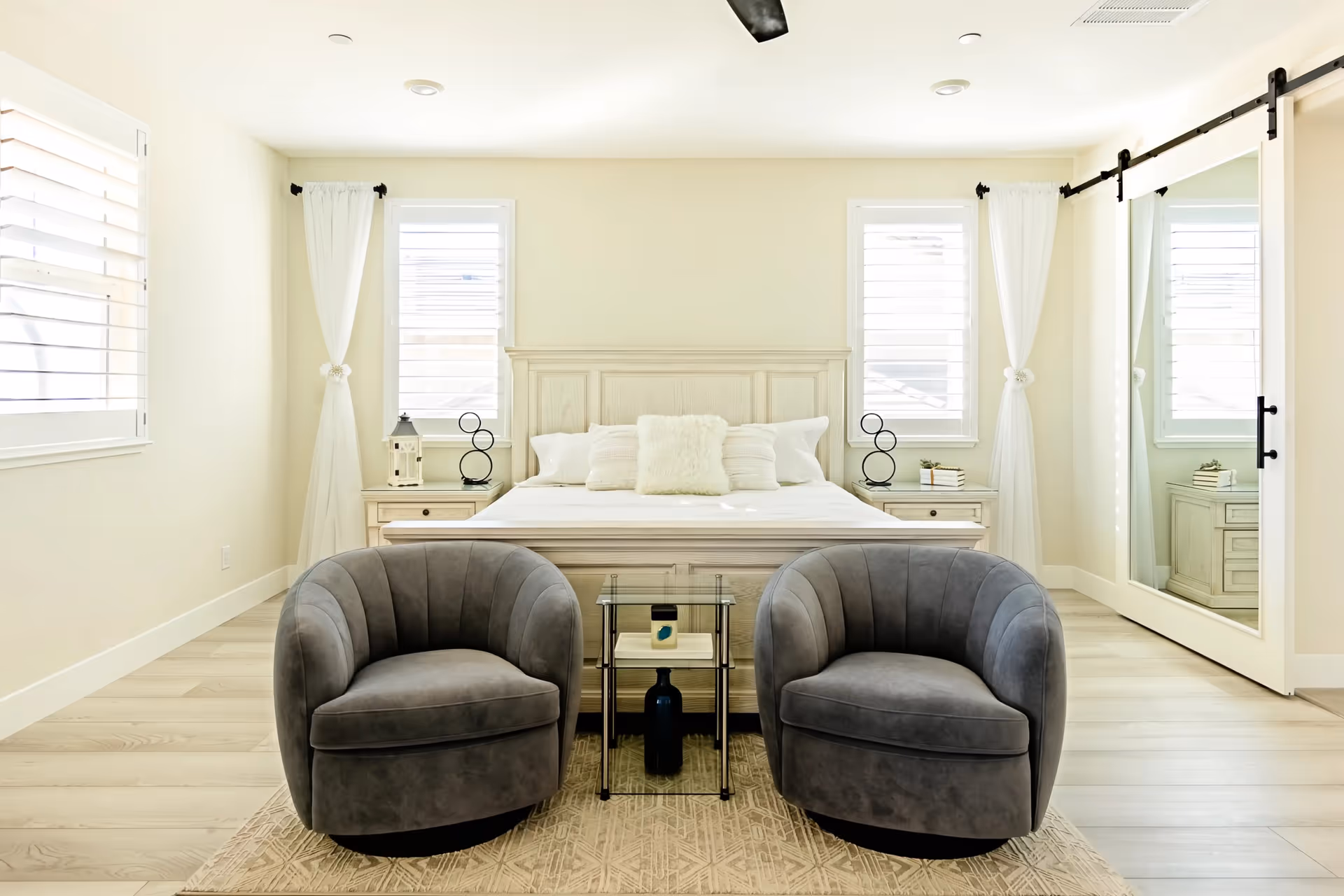 Bright, minimalist bedroom with a white bed, two nightstands, and two gray armchairs.