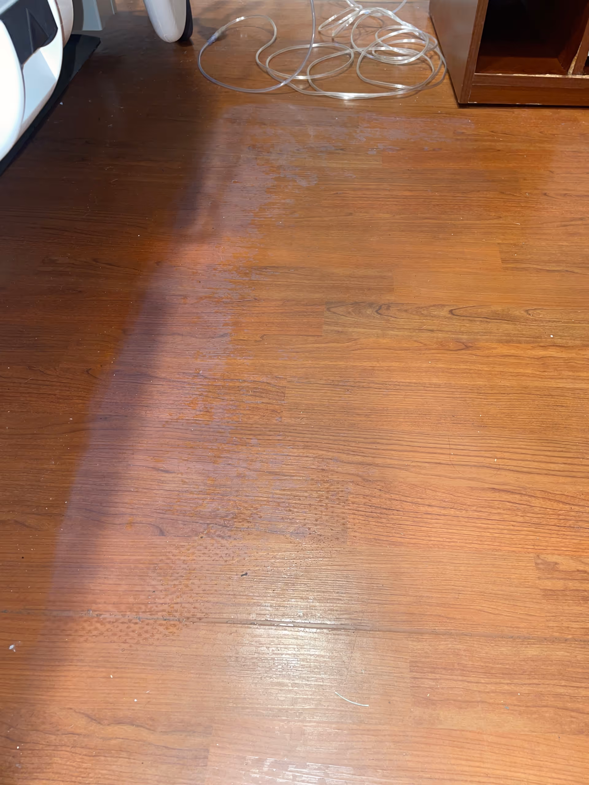 Wood floor with tangled cords and cabinet edge in an indoor room.