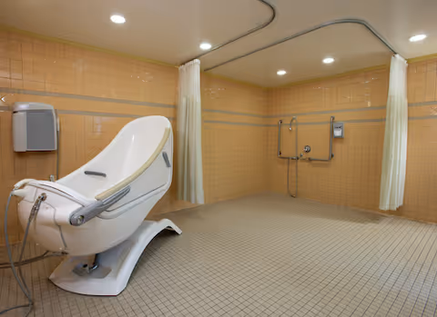 Orange-tiled accessible bathroom with a reclining spa chair and curtained shower stalls.