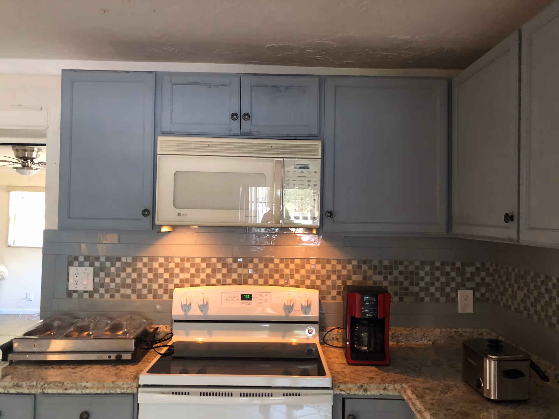 Blue kitchen cabinets frame a microwave, stove, and coffee maker against a tiled backsplash.