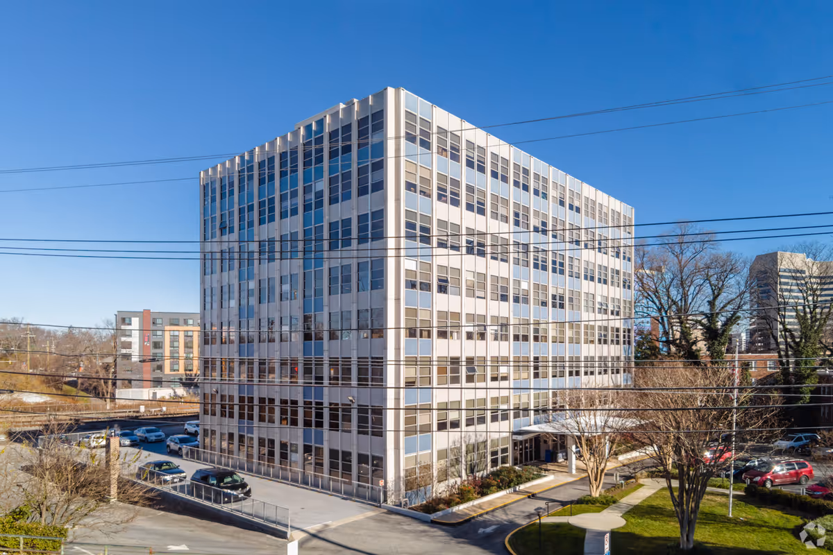 A tall modern building exterior with glass windows and surrounding parking lot.