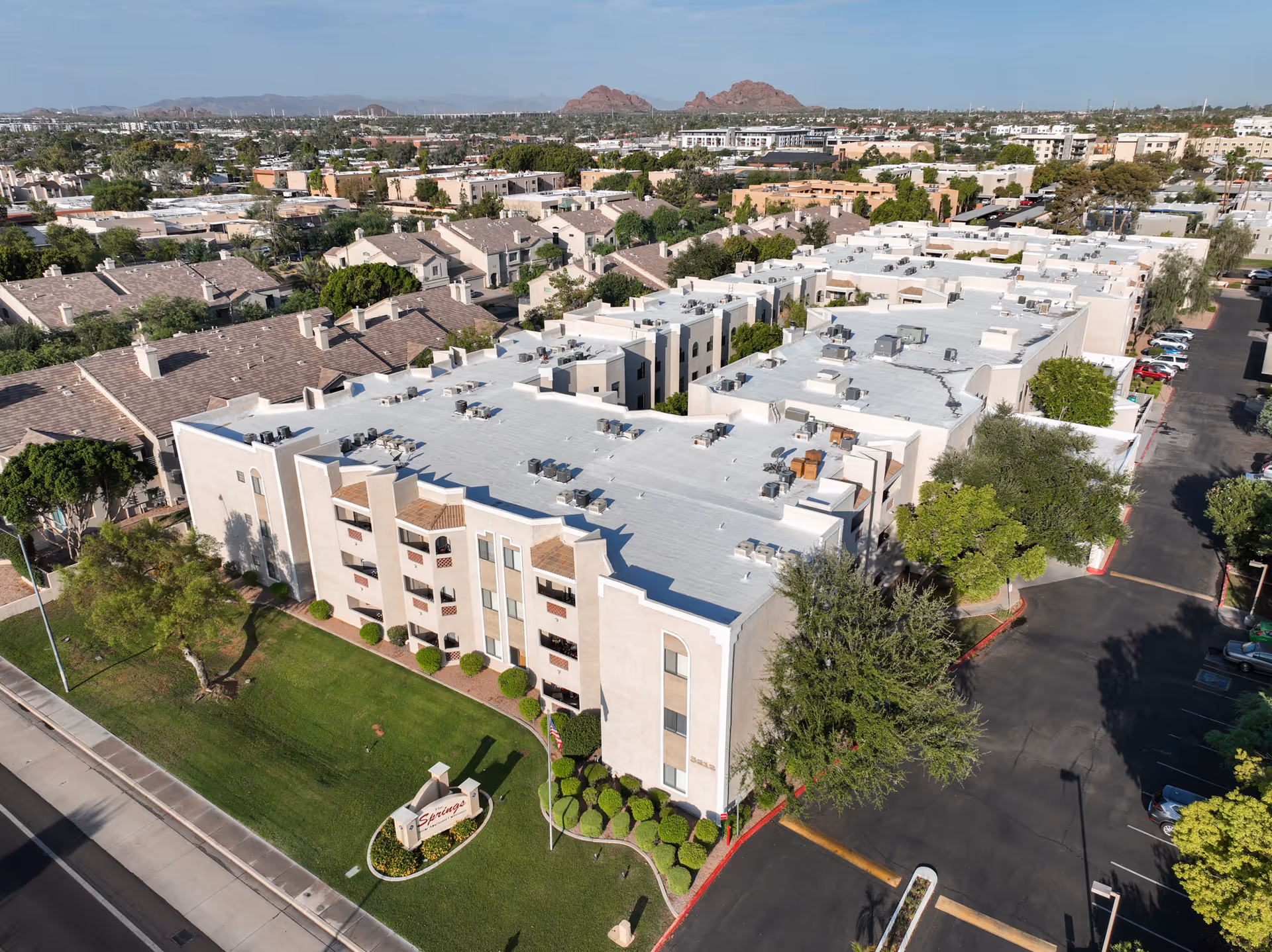 Aerial view of a light-colored senior living campus with manicured lawn and surrounding streets