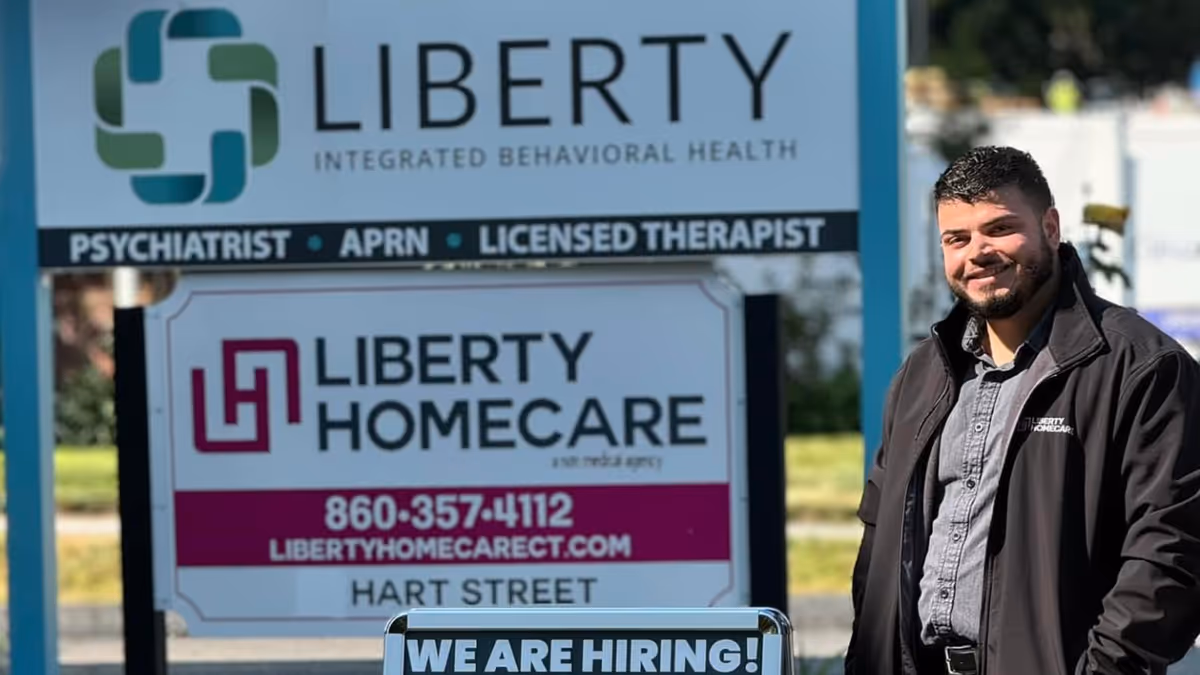 A man stands beside a Liberty Homecare sign outdoors, with 'We are hiring' visible.