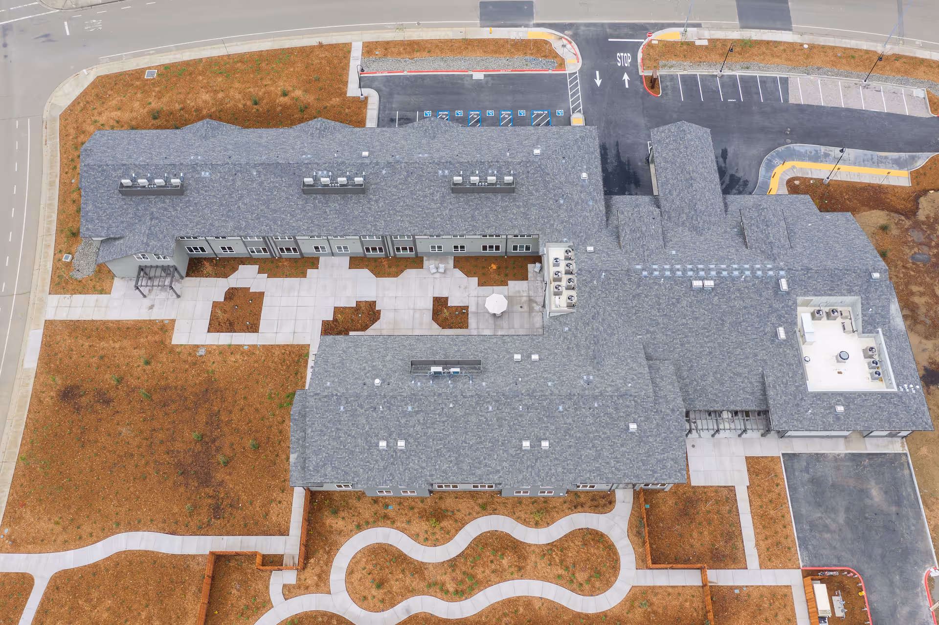Aerial view of Vine Ridge Senior Living building with grey roof, parking, and winding walkways.