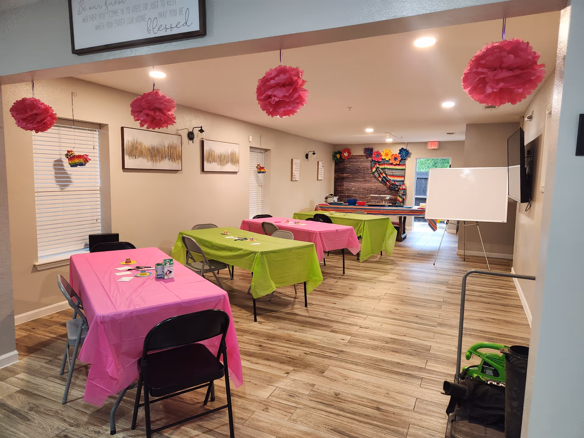 Brightly colored tables with pink and green tablecloths arranged for activities in a community room.