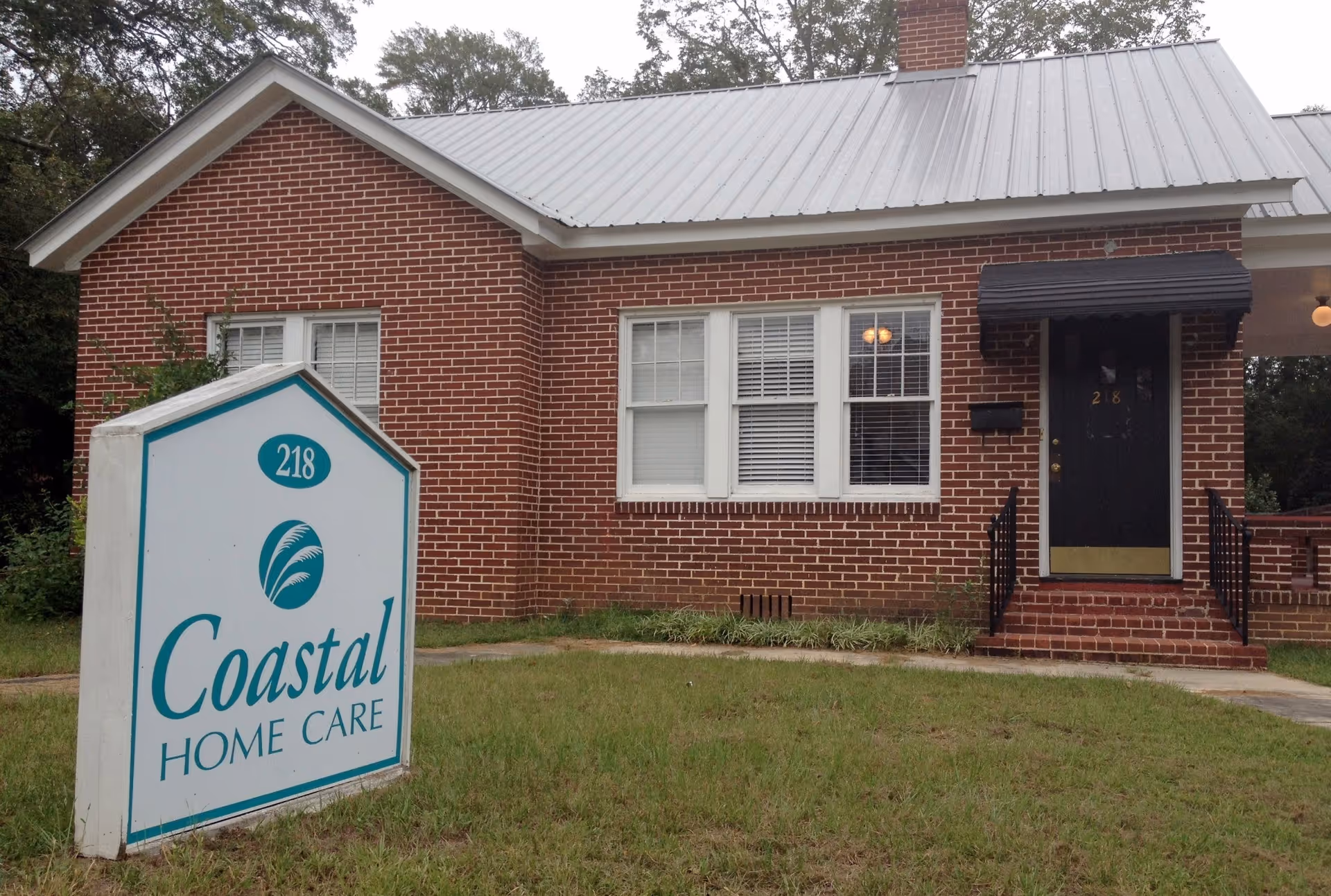 Brick building with a front entrance and Coastal Home Care sign in grassy yard