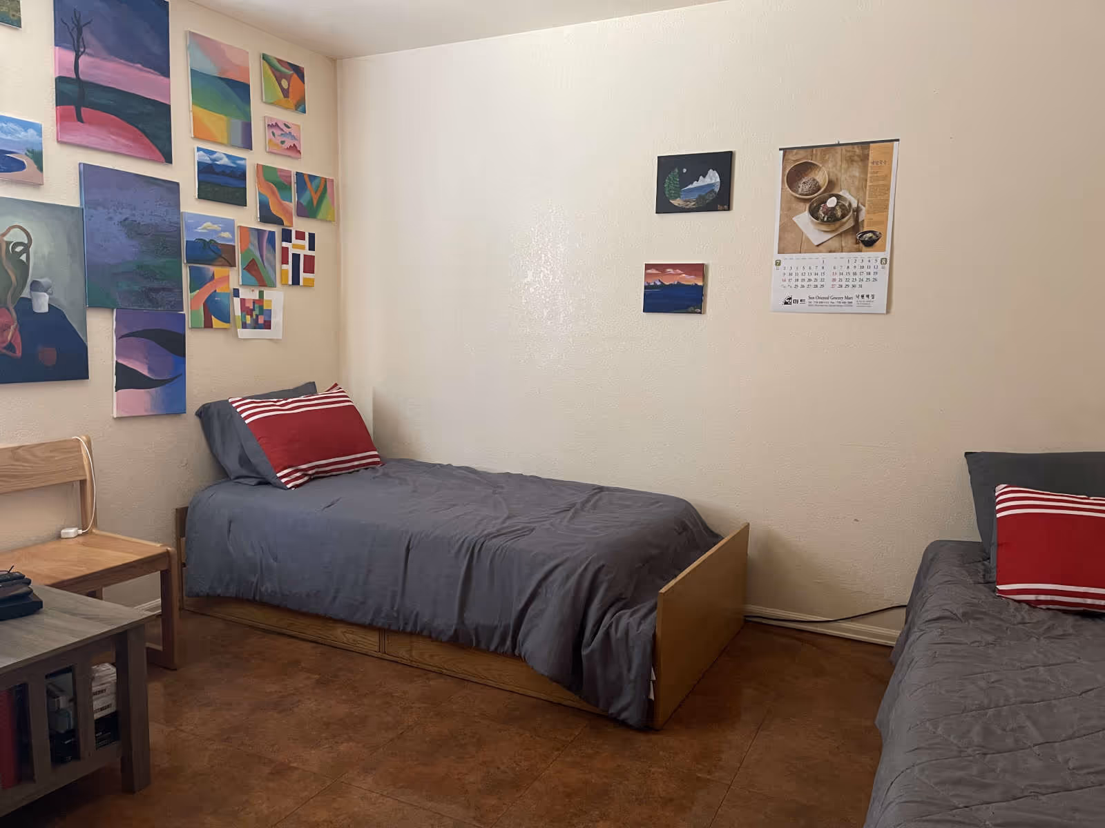 Two twin beds with gray bedding and colorful wall art in a small room.