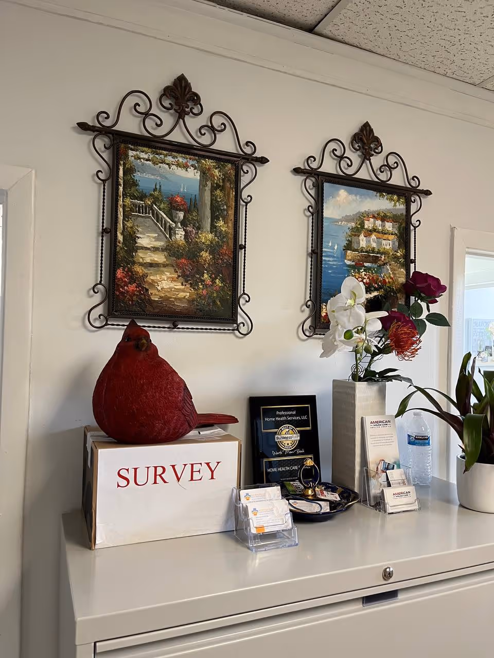 Indoor reception desk area with framed artwork, flowers, and a red cardinal sculpture.