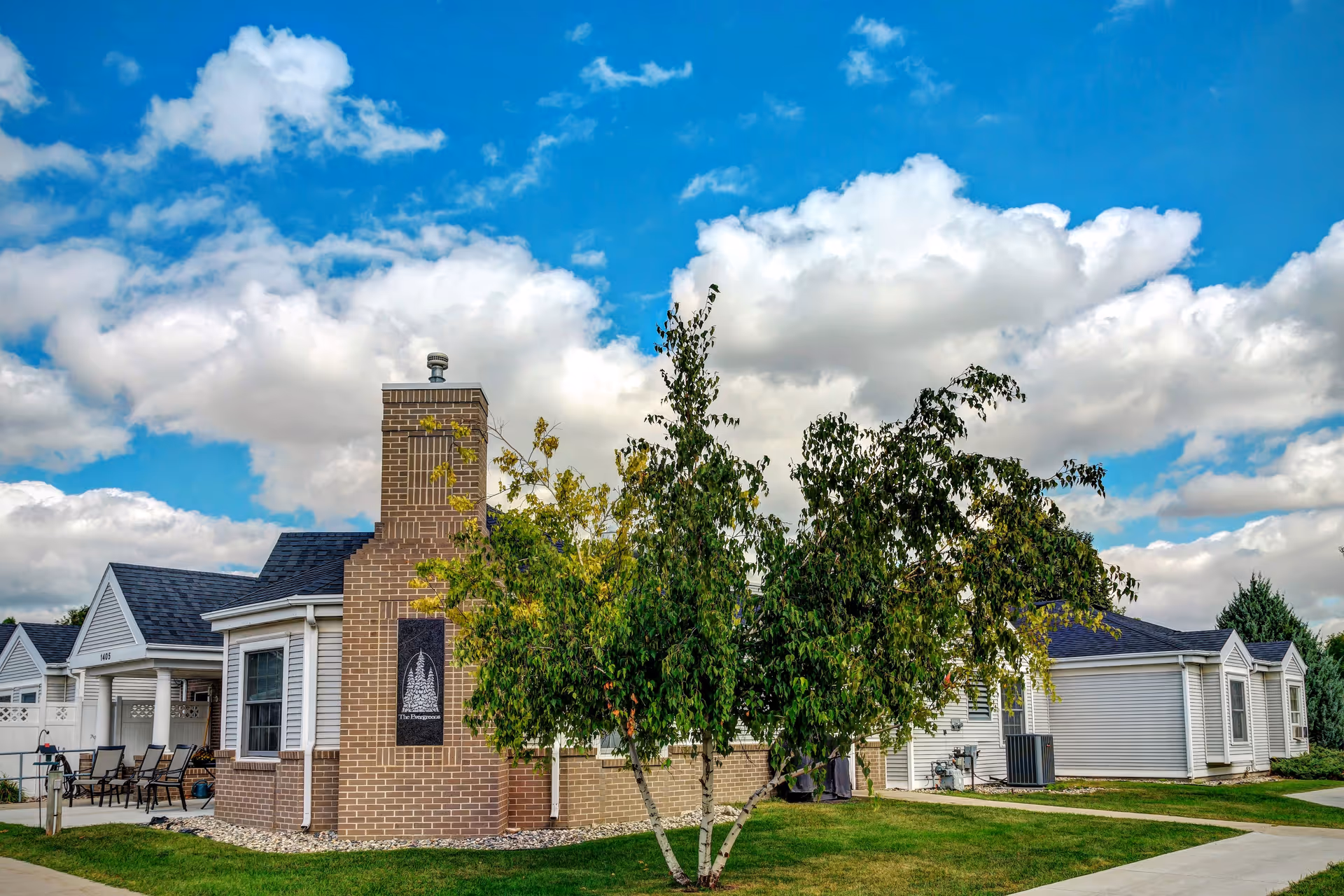Exterior view of Ecumen Evergreens of Fargo with brick chimney, trees, and patio seating.