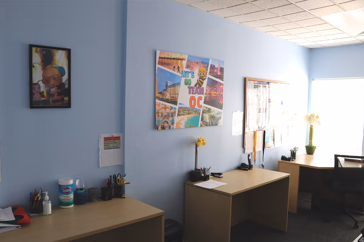 Office workspace with light blue walls, desks, posters, and office supplies.
