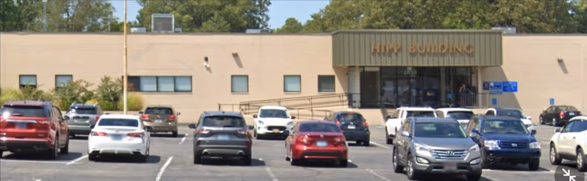 Front view of a beige building with a parking lot full of cars.