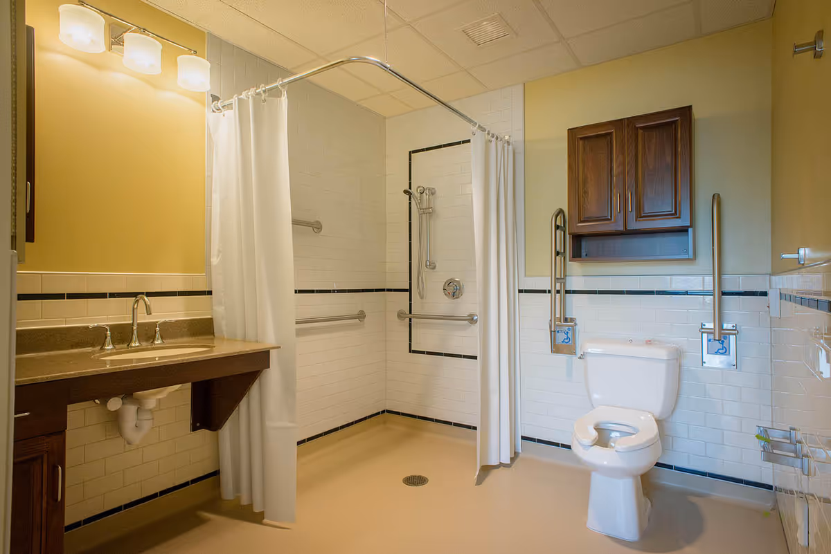 Accessible bathroom with shower, toilet, sink, and grab bars in memory care facility.