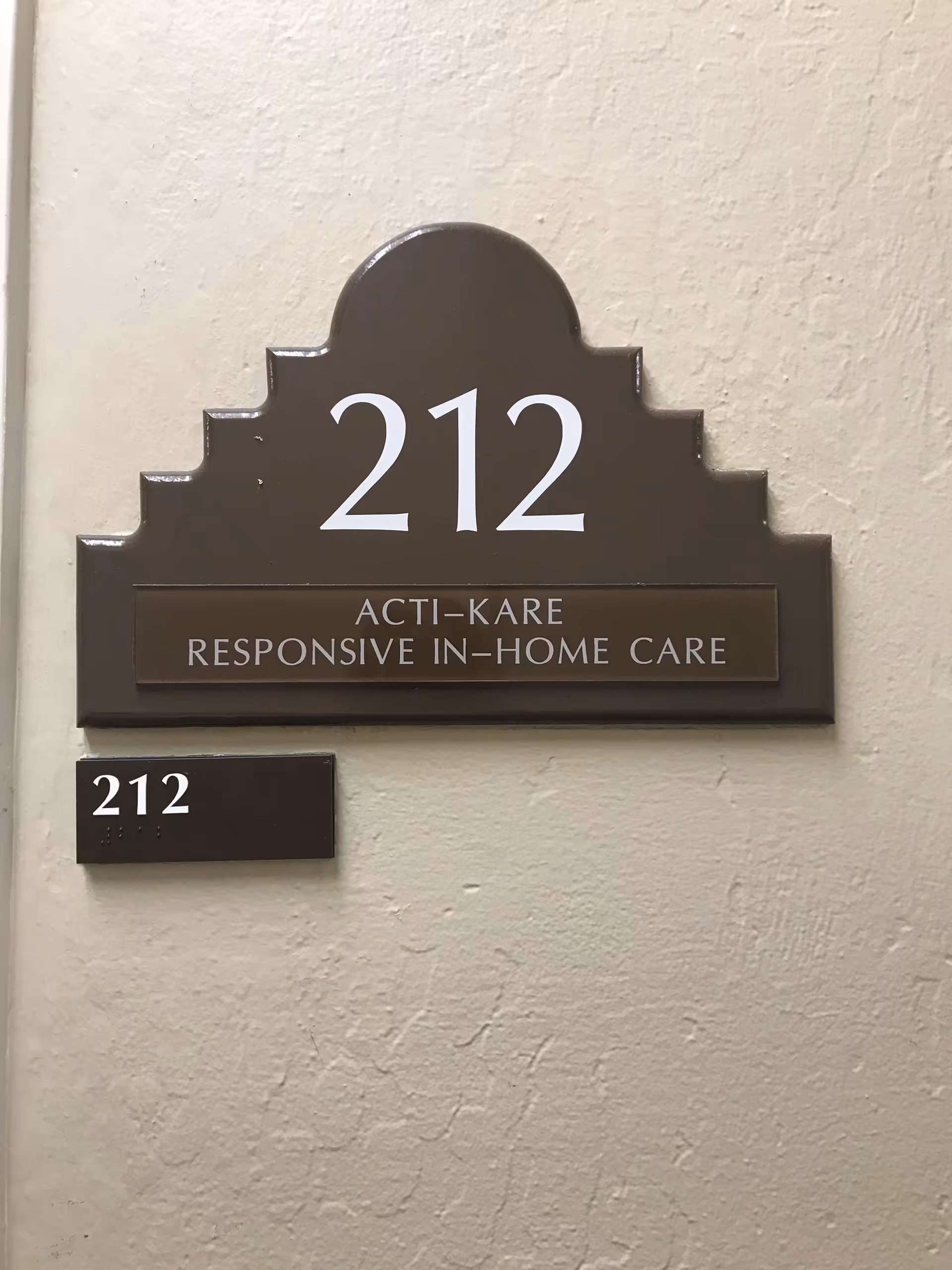 Decorative brown plaque on a wall displays 212 and Acti-Kare in-home care.