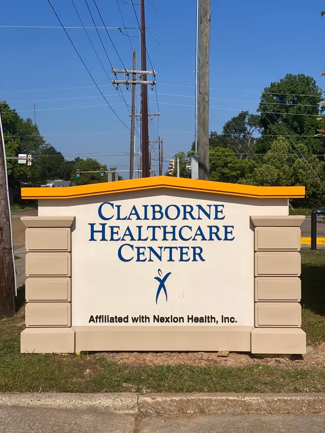 A freestanding outdoor entrance sign that reads "Claiborne Healthcare Center" with a yellow top and an affiliation line below.