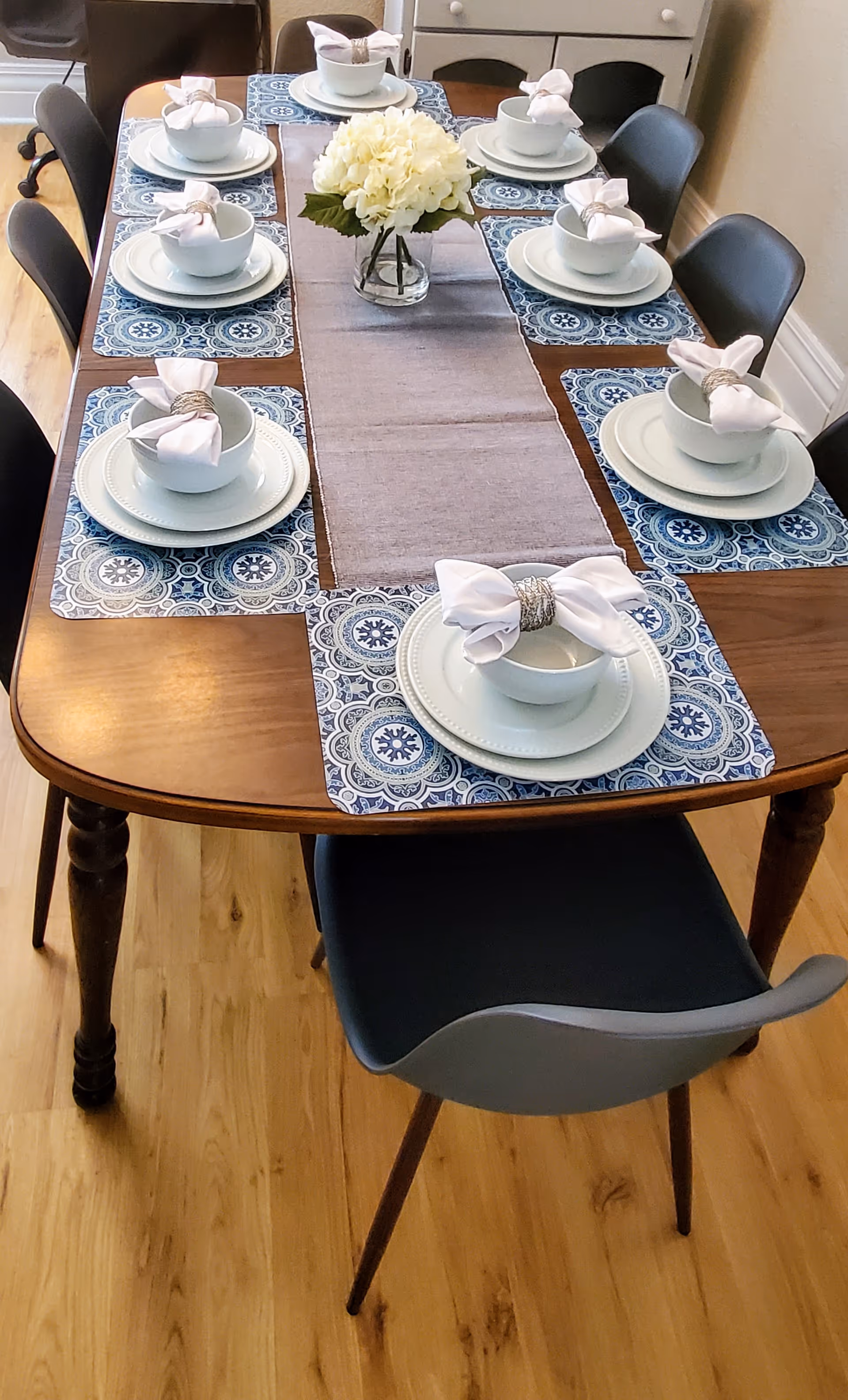 Dining table set for six with plates, bowls, napkins, and a floral centerpiece.