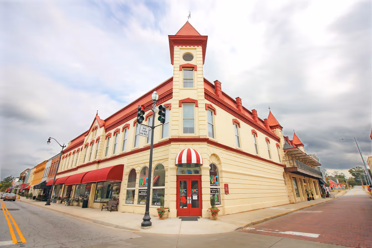 Exterior view of a cream building with red trim and arched windows on a street.