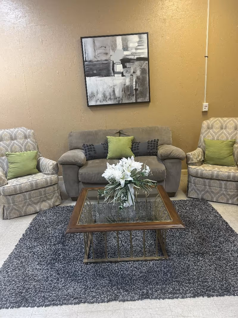 Neutral-toned living room with sofa, two armchairs, glass coffee table, rug, and abstract artwork.