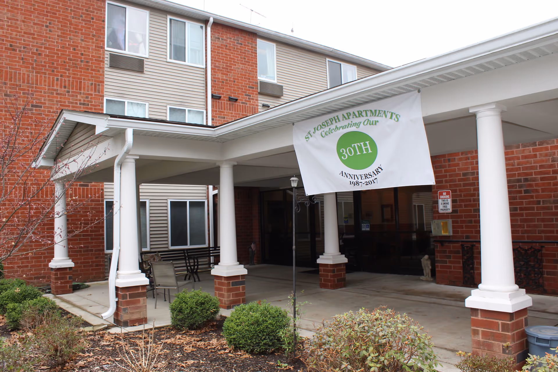 Exterior view of St Joseph Apartments entrance with white columns and anniversary banner.