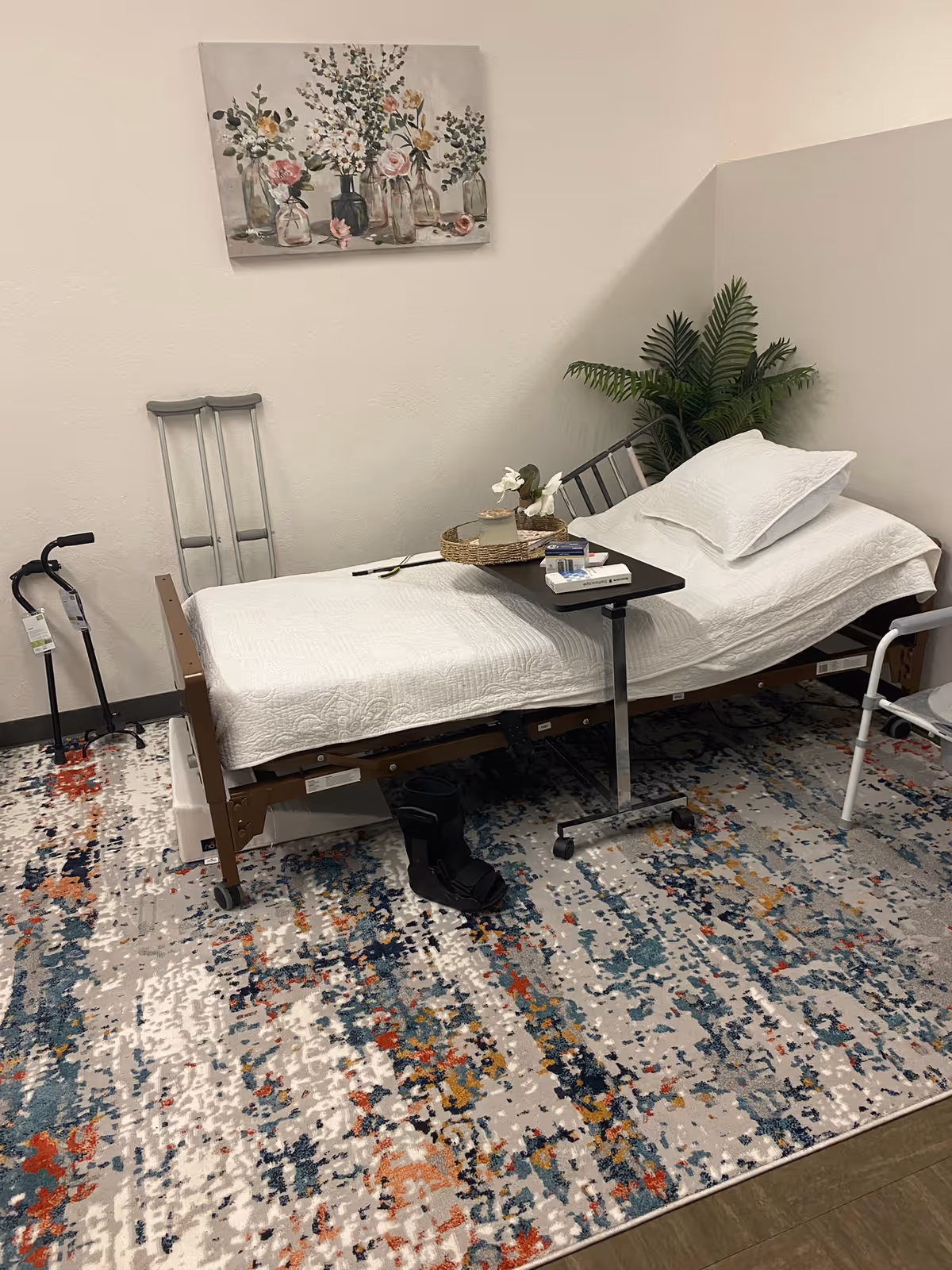 A hospital-style adjustable bed in a furnished patient room with a small table and decor.