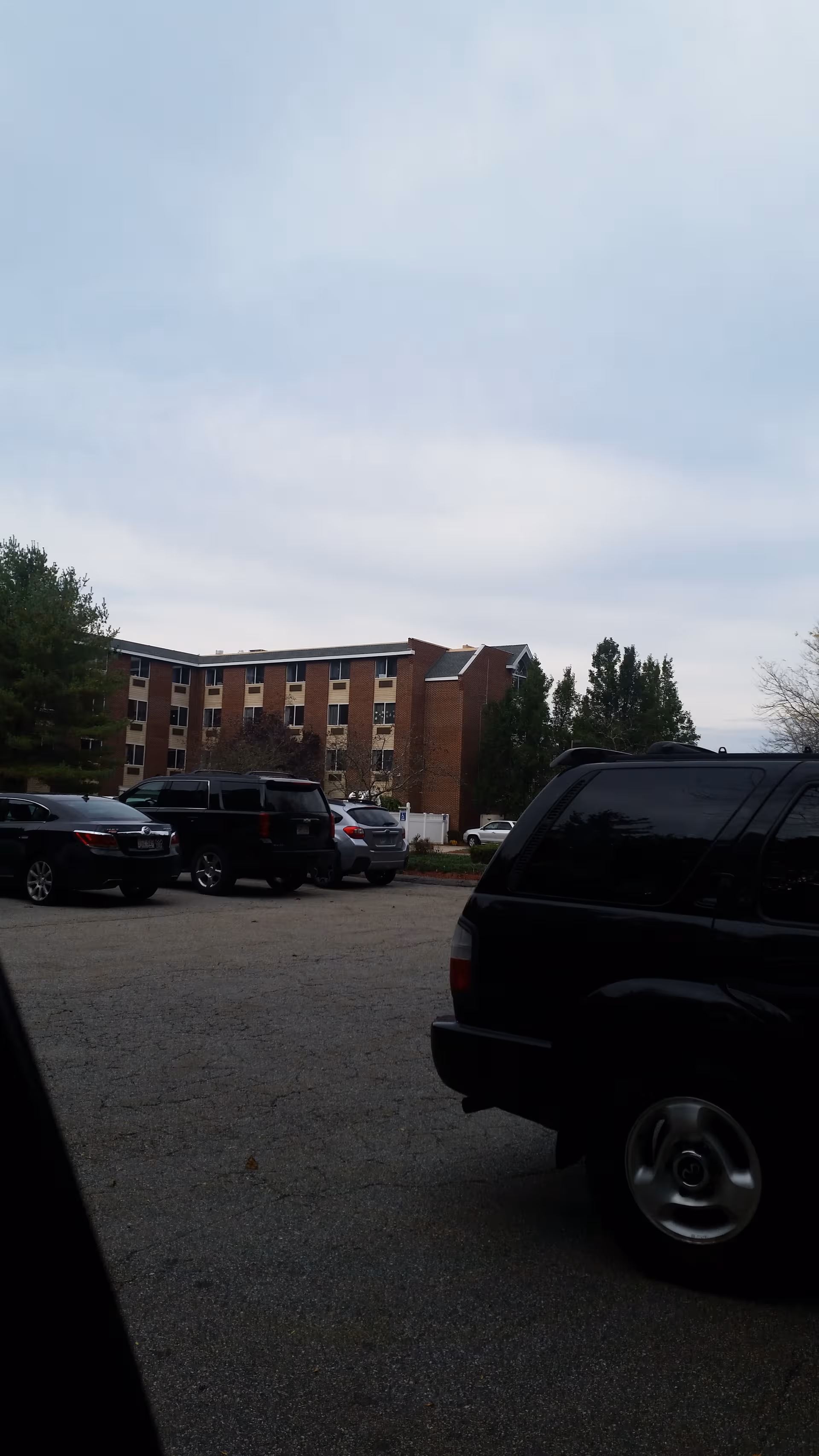 Exterior view of a brick senior facility with a parking lot and cars.