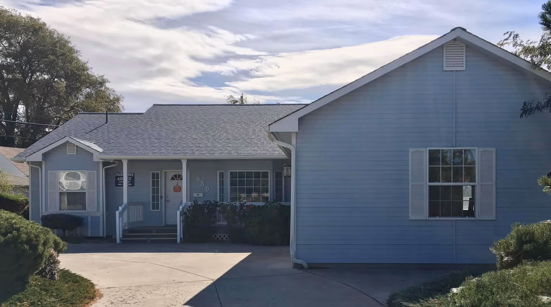 Blue single-story building with a front entrance, porch, and landscaped shrubs.