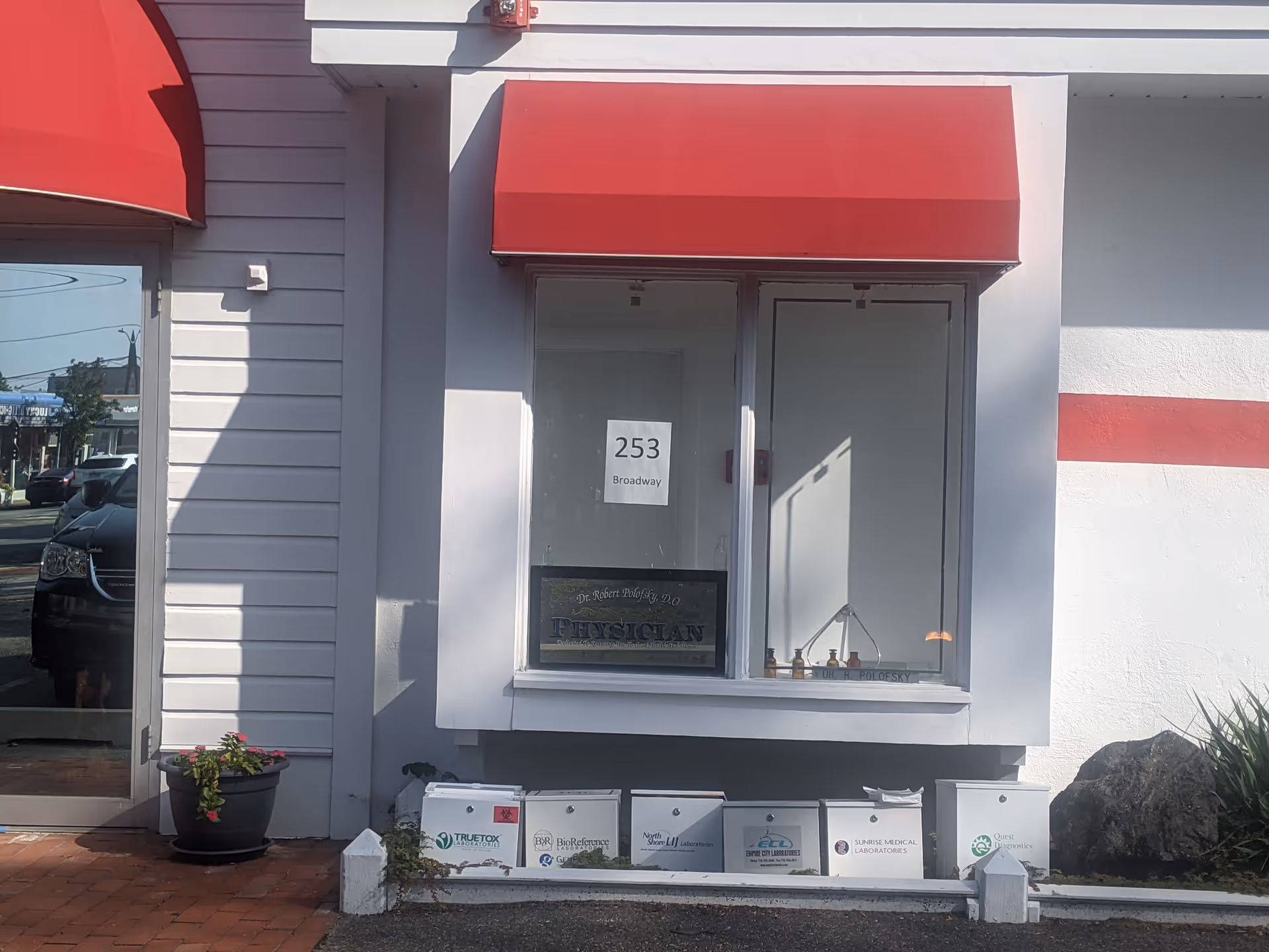 Exterior storefront with red awning and window sign 253 Broadway, row of mailboxes below.