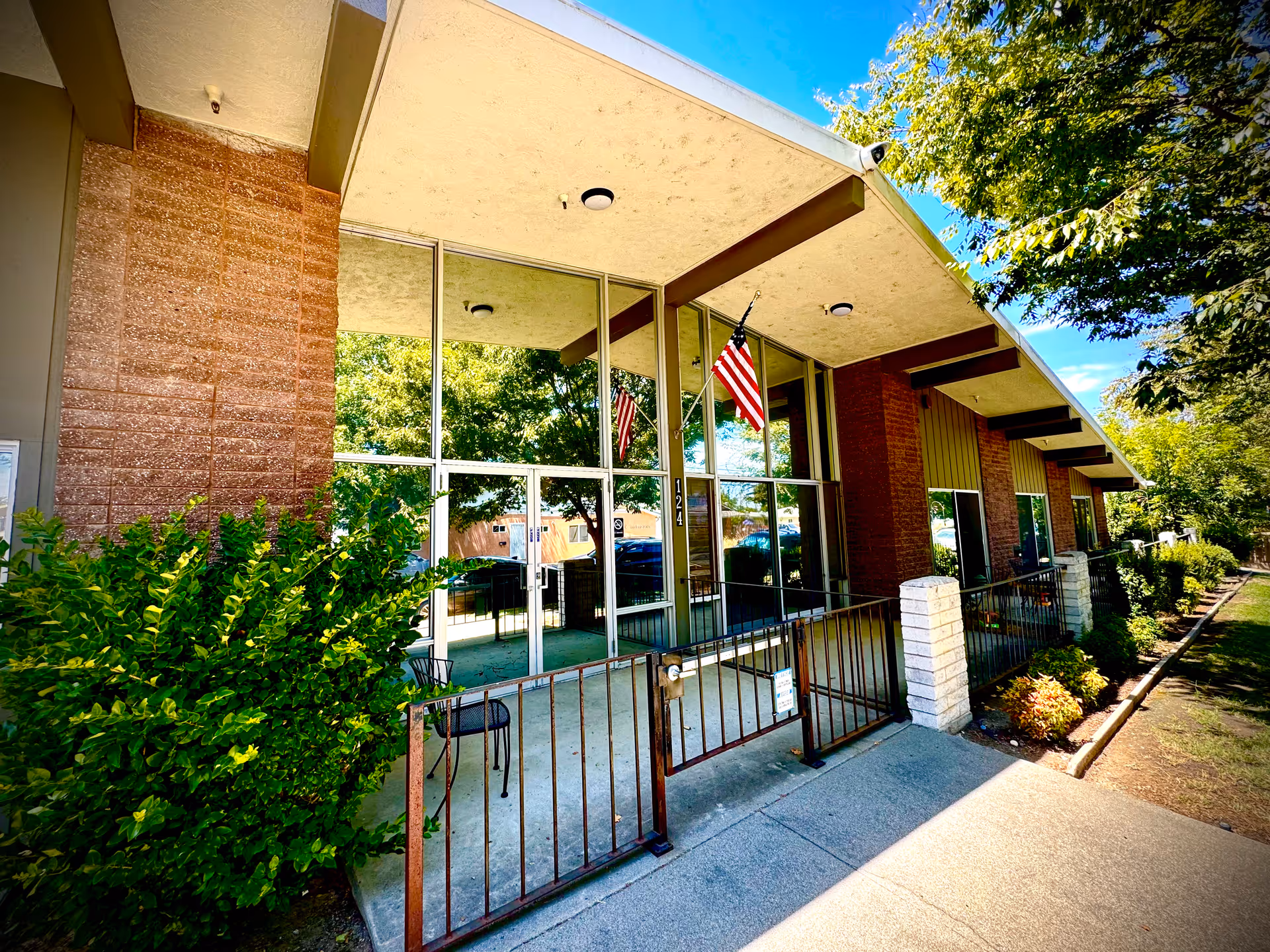 Front exterior of a facility with glass entry, flags, and landscaping.
