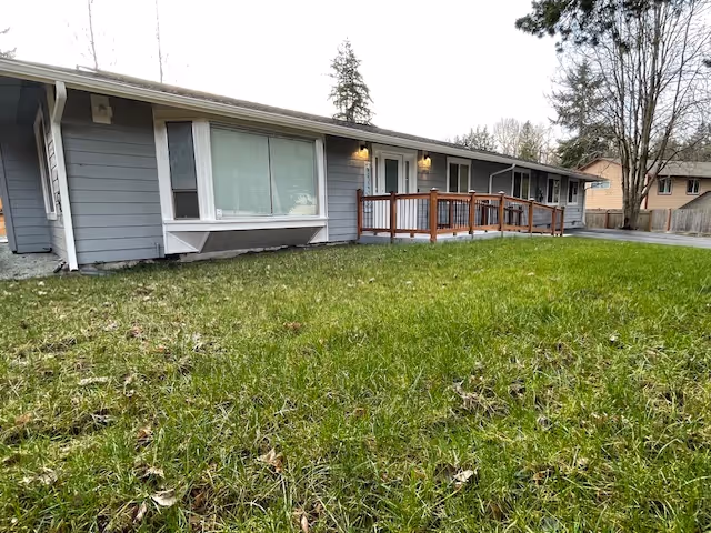 Single-story senior facility with gray siding, large front windows, and a wooden ramp.