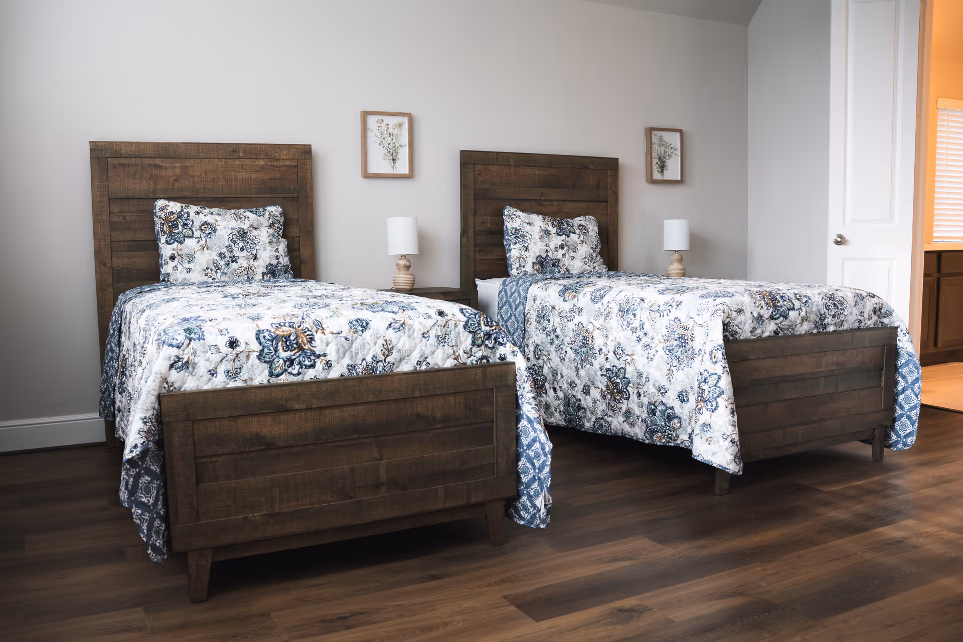 Two wooden twin beds with floral bedding sit in a neutral, well-lit bedroom.