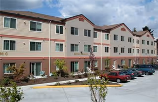 Sunset Gardens senior living facility exterior with beige siding, brick base, and parked cars.
