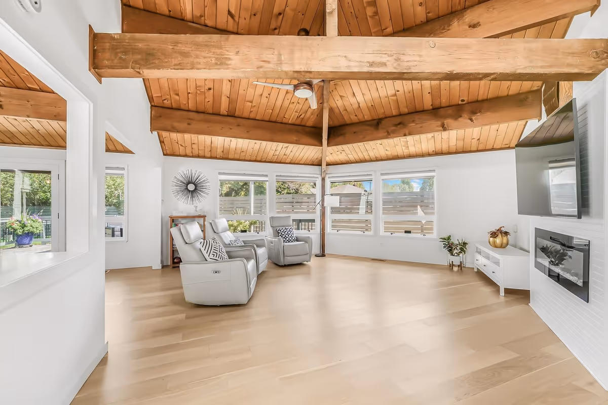 Bright living room with wooden beam ceiling, large windows, and white recliners.
