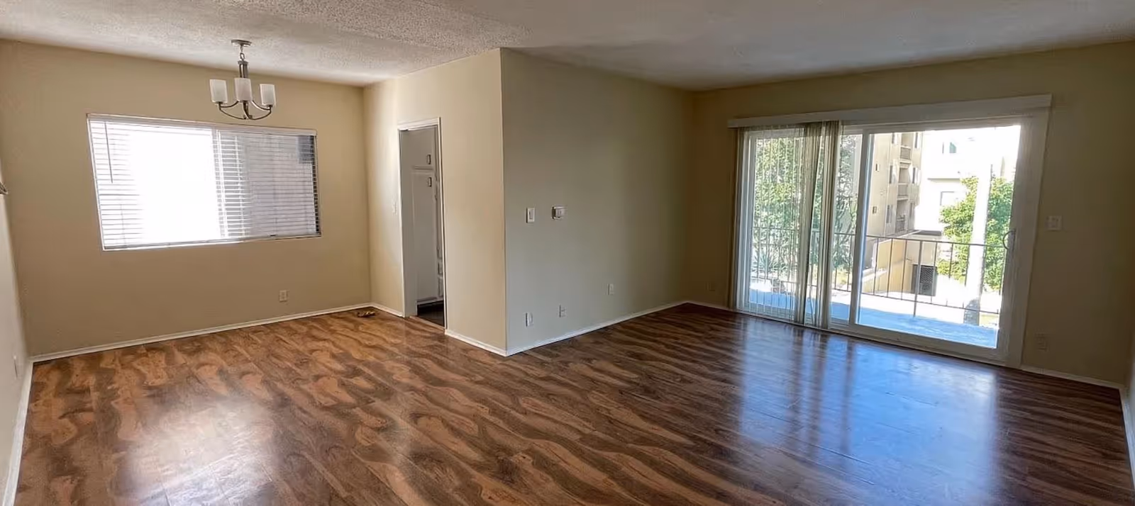 Bright, empty living room with wood floors, sliding glass door, and balcony window.