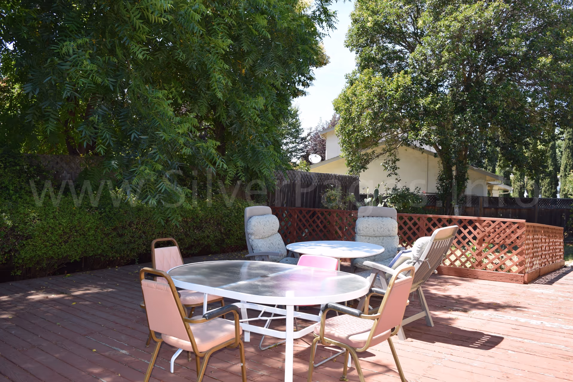 Outdoor patio with round table and chairs, surrounded by trees and a fenced yard.