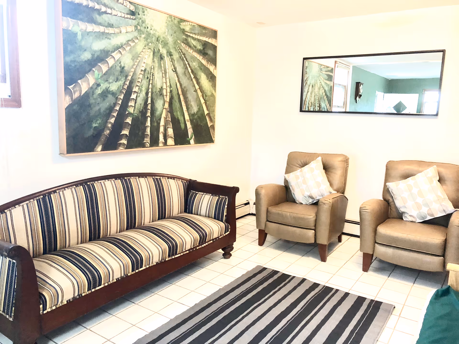 A bright common living room with striped sofa, two beige armchairs, and wall art.