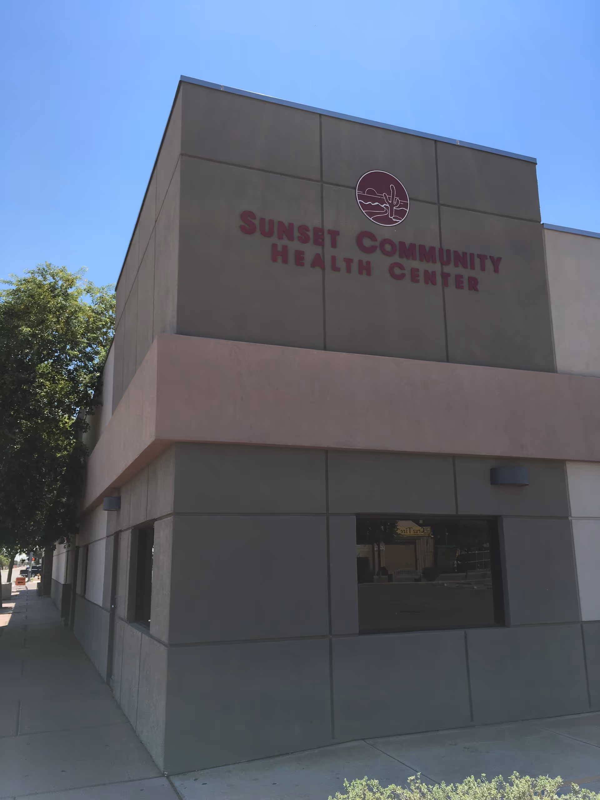 Exterior view of Sunset Community Health Center building with pink signage on gray walls.