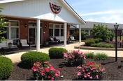 Front entrance of Logan Elm Health Care Center with a covered porch and residents seated.