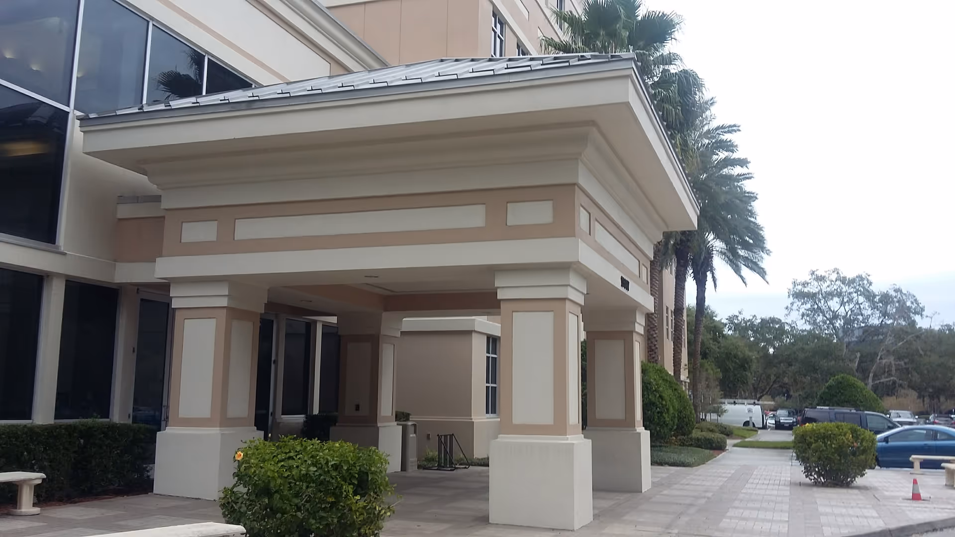 Entrance of a beige senior living facility with a covered porte-cochere and palm trees.