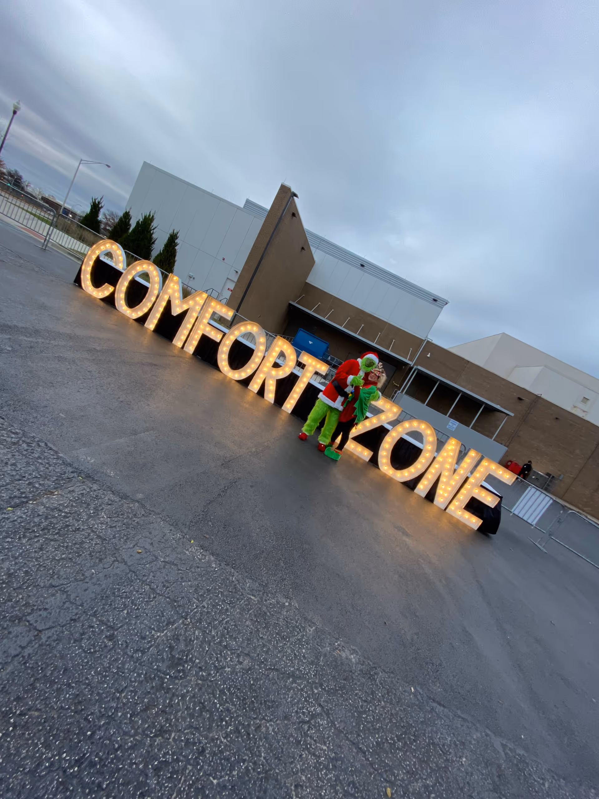 Exterior of a building with illuminated COMFORT ZONE sign and costumed figure near entrance.