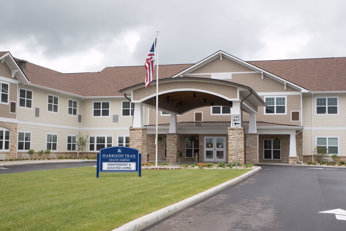 Front entrance of Harrison Trail Health Campus with a covered porte-cochere, American flag, and a sign for independent & assisted living.